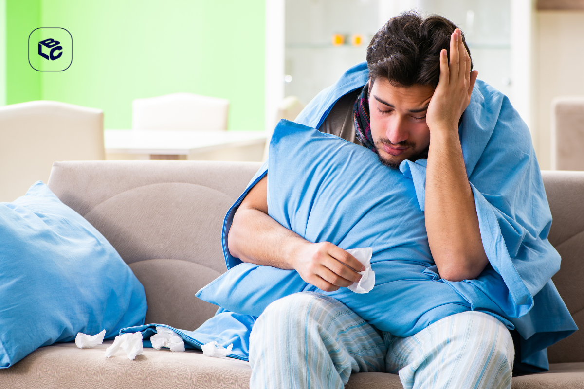 Homem doente coberto com cobertor azul abraçando travesseiro, segurando lenço de papel